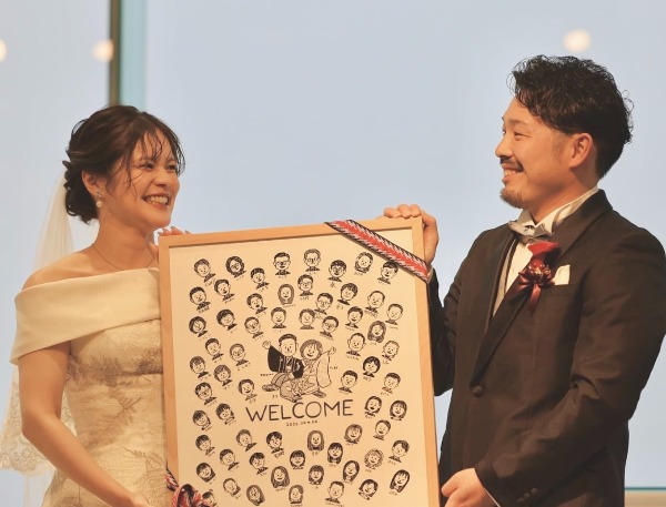 お世話になっております。

この度は、結婚証明書を作成いただき、誠にありがとうございました。
式から1週間が経ち、ようやく落ち着いてきたため、改めて感謝の気持ちをご連絡させていただきます。

結婚式をすると決める前に、ぐりこさまの結婚証明書を拝見して以来、
もし式をするならば絶対にお願いしたい！と思っておりました。
そのため、抽選と知った時は不安で仕方がありませんでしたが
藁にもすがる思いで応募し、当選のメールをいただいた時は
飛び上がるほど嬉しかったです！

当日、ゲストに名前を書き入れてもらい無事完成しました。
ゲストが似顔絵を見ながらわいわいしてる様子がとても微笑ましかったので、
写真も共有させていただきます。

本当に素敵な結婚証明書に仕上げていただき
心より感謝申し上げます。

皆様の今後のさらなるご活躍をお祈りしております。